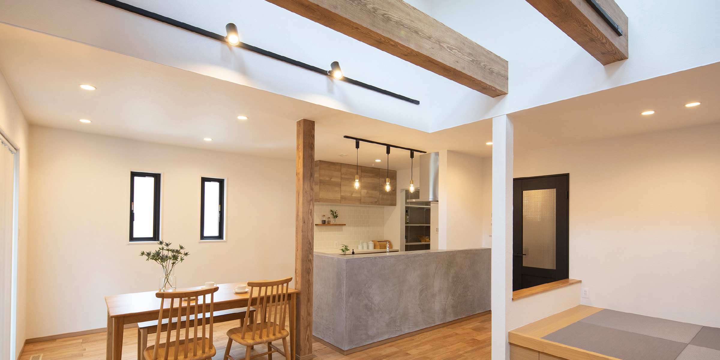 吹き抜けの大きな梁や木製の家具、モルタルのキッチンなど、ナチュラルで優しい雰囲気のリビング・ダイニング